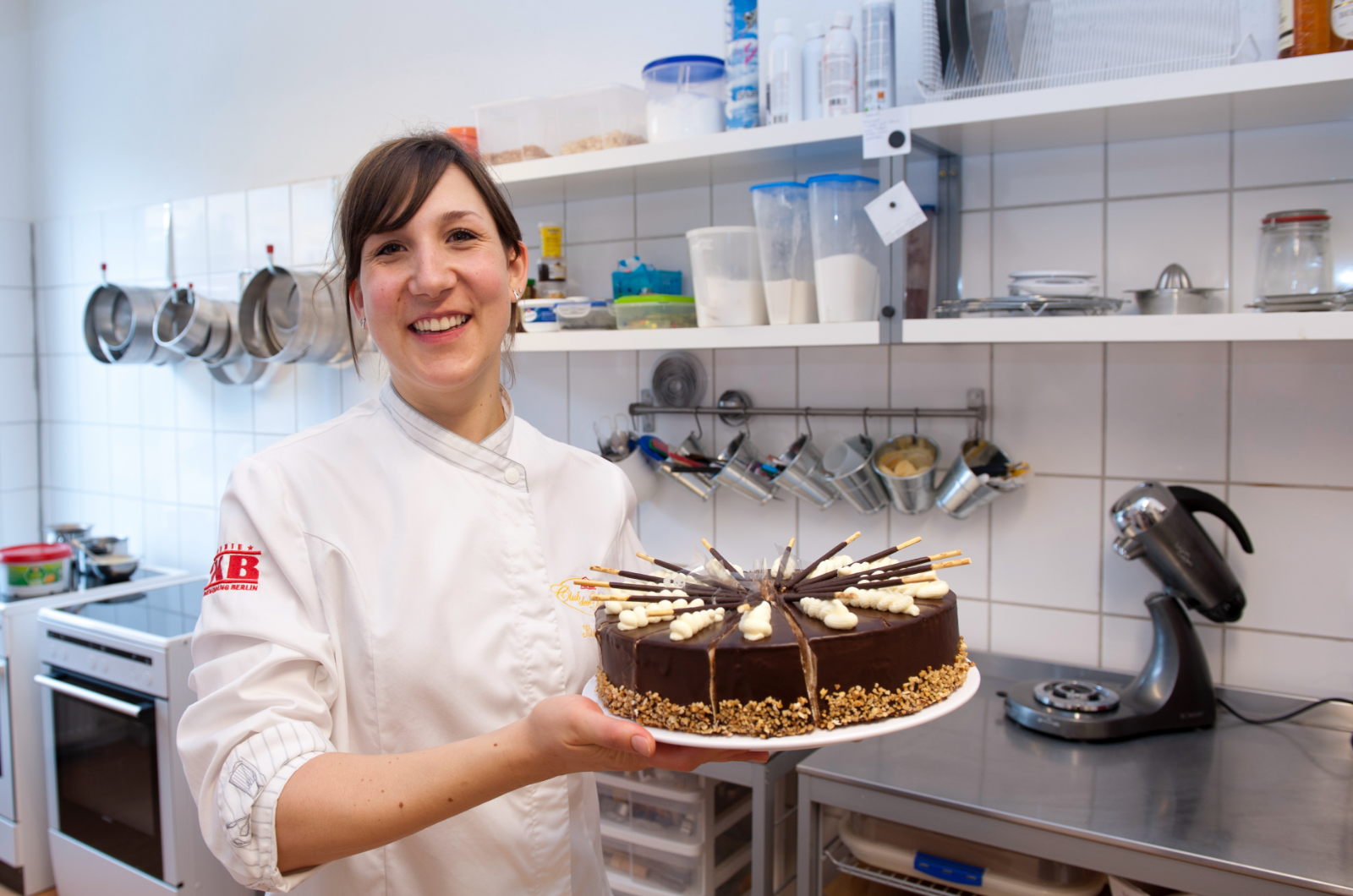 Junge Mitarbeiterin in einer Großküche präsentiert lächelnd eine Torte.